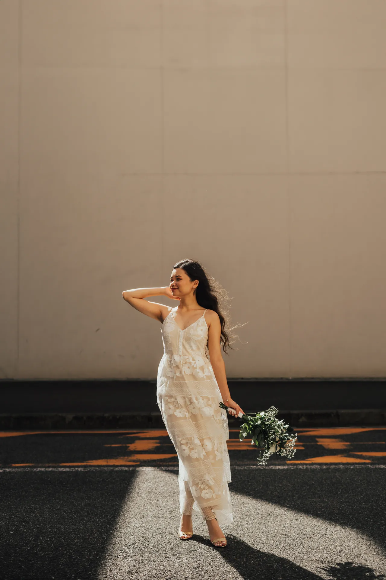 Noiva de vestido de renda caminhando ao sol com um buquê na mão