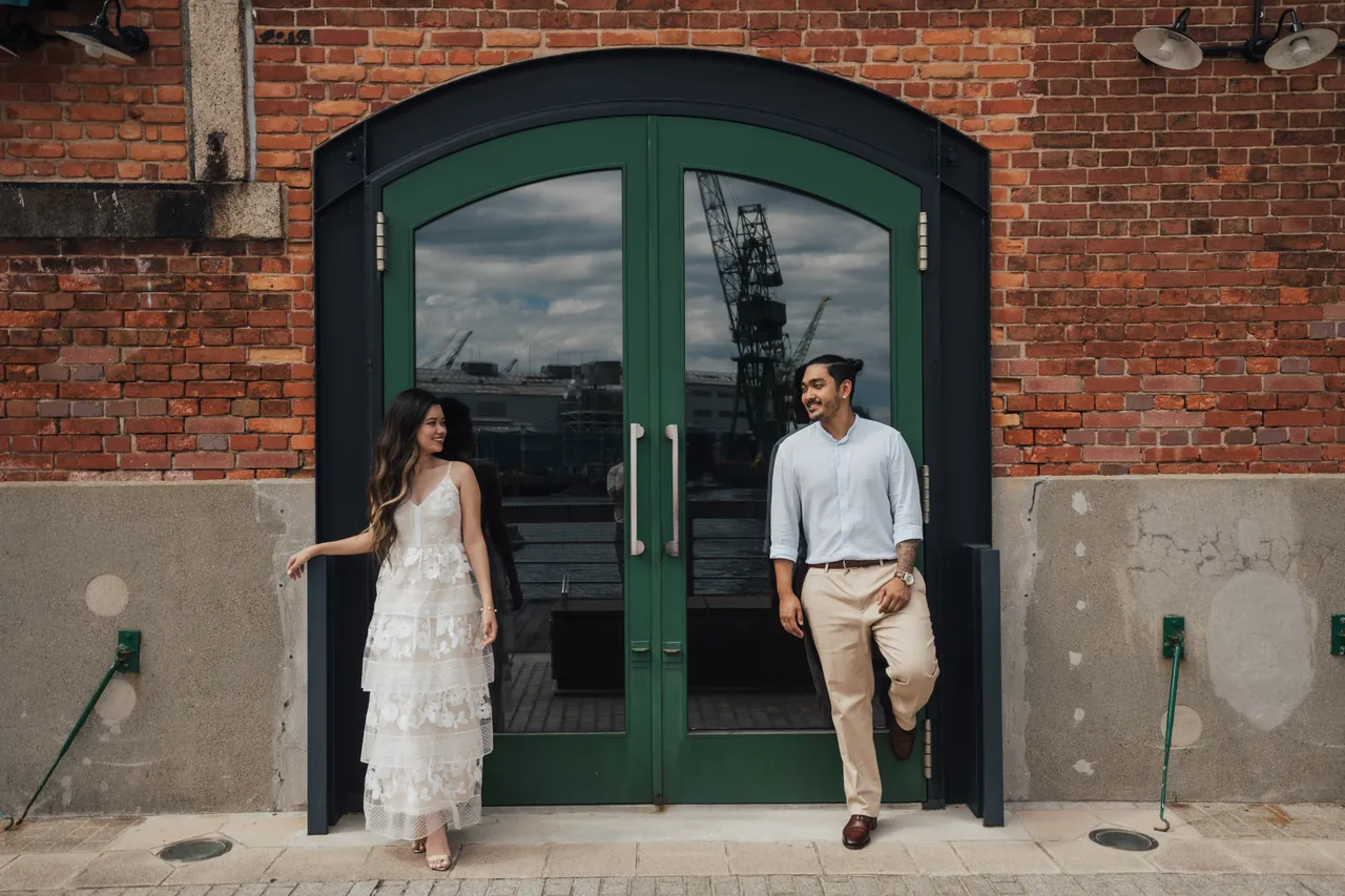 Casal diante de uma porta verde num prédio de tijolos vermelhos