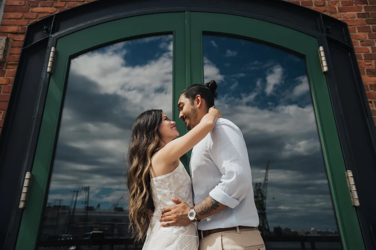 Casal abraçado diante de uma porta de vidro que reflete as nuvens