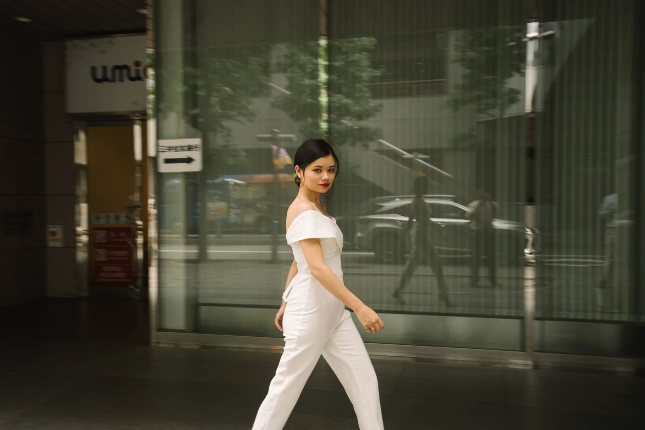 Mulher de branco caminhando diante de uma fachada de vidro